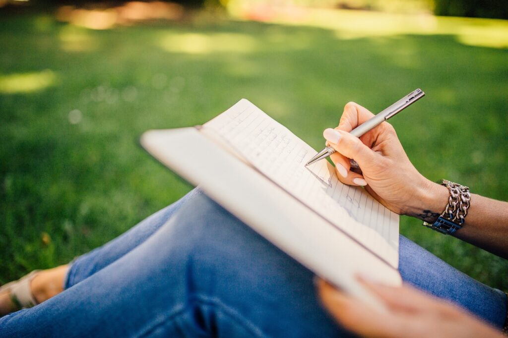 Woman writing in open notebook while sitting in grass.
